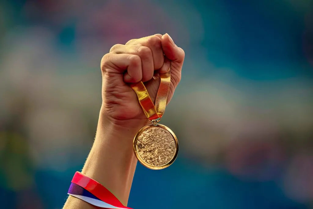 Mão segurando medalha olímpica, simbolizando vitórias nas Olimpíadas e o impacto da arquitetura francesa no evento.